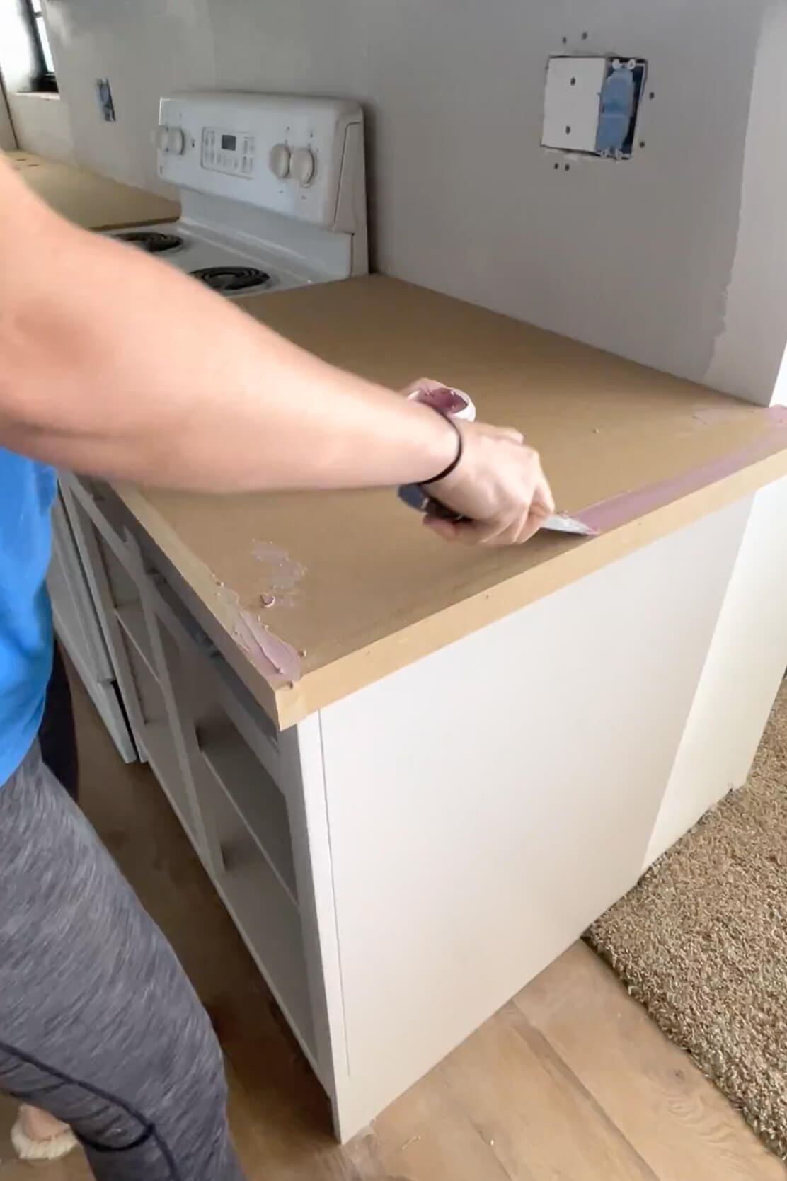 Using wood filler to fill in seams and nail holes in a DIY kitchen countertop.